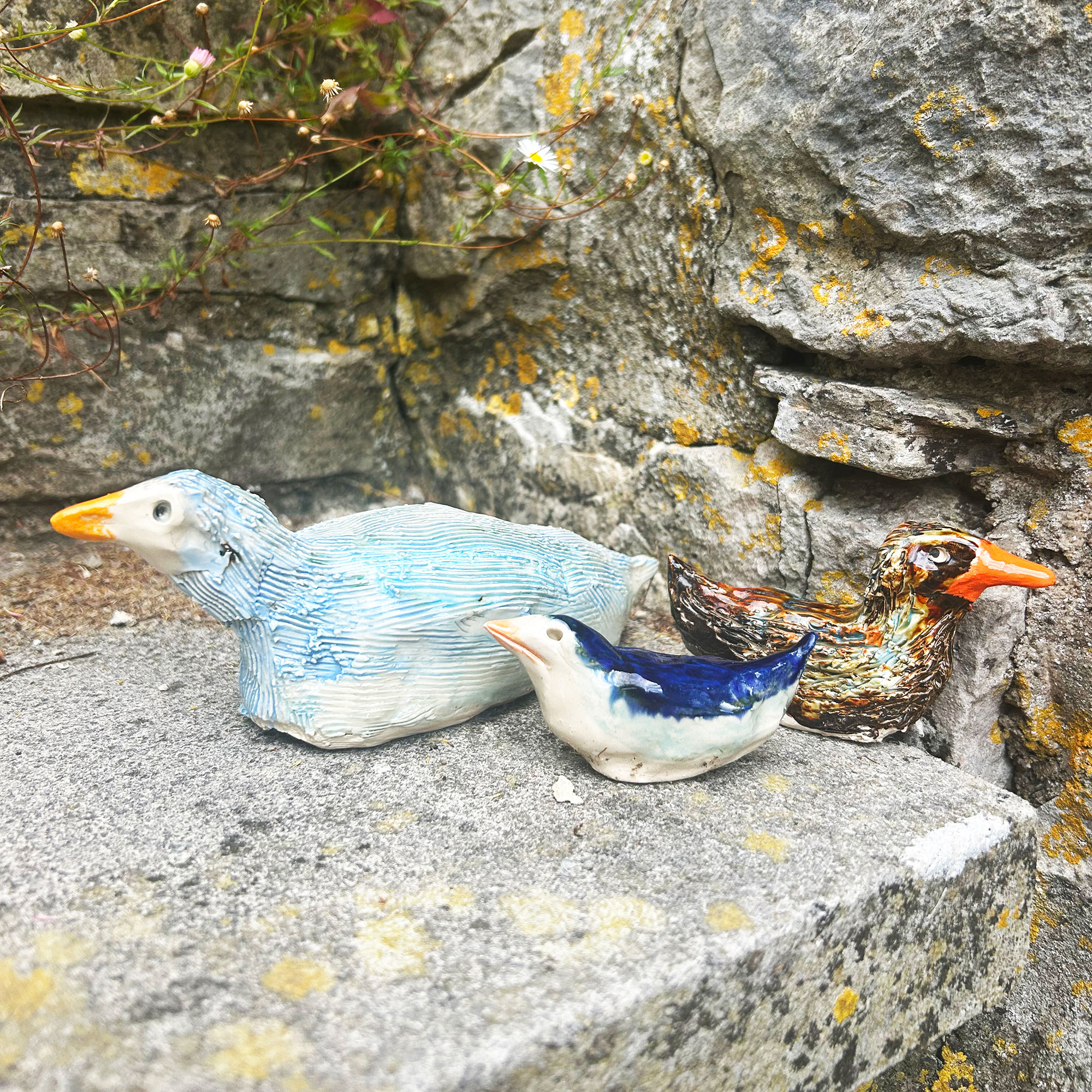 Three painted and glazed ceramic birds on stone step beside stone wall