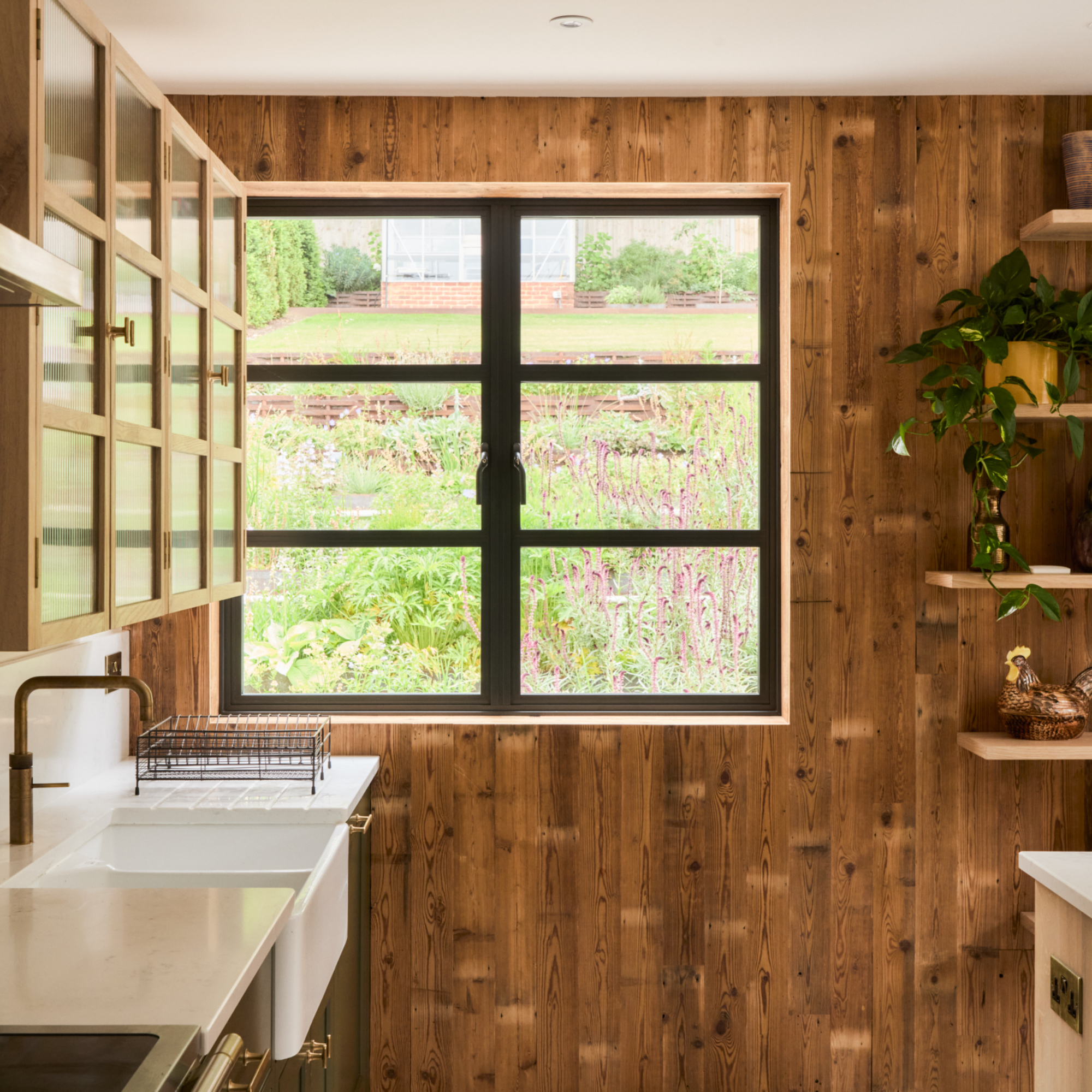 kitchen with wood paneling, glazed wall unit, white work tops, view to garden