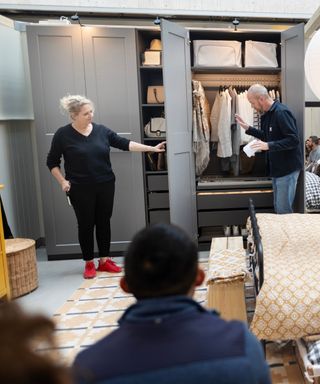 Two IKEA workers revealing the inside of an organized closet with gray doors.