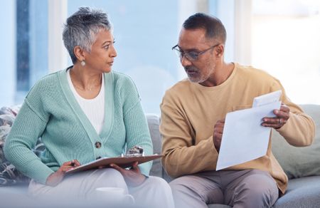 A woman holds a clipboard filling out a form while a man looks at another piece of paper.