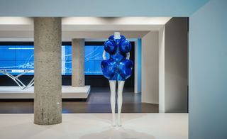 mannequin wearing a bright blue dress in a art gallery with concrete pillars