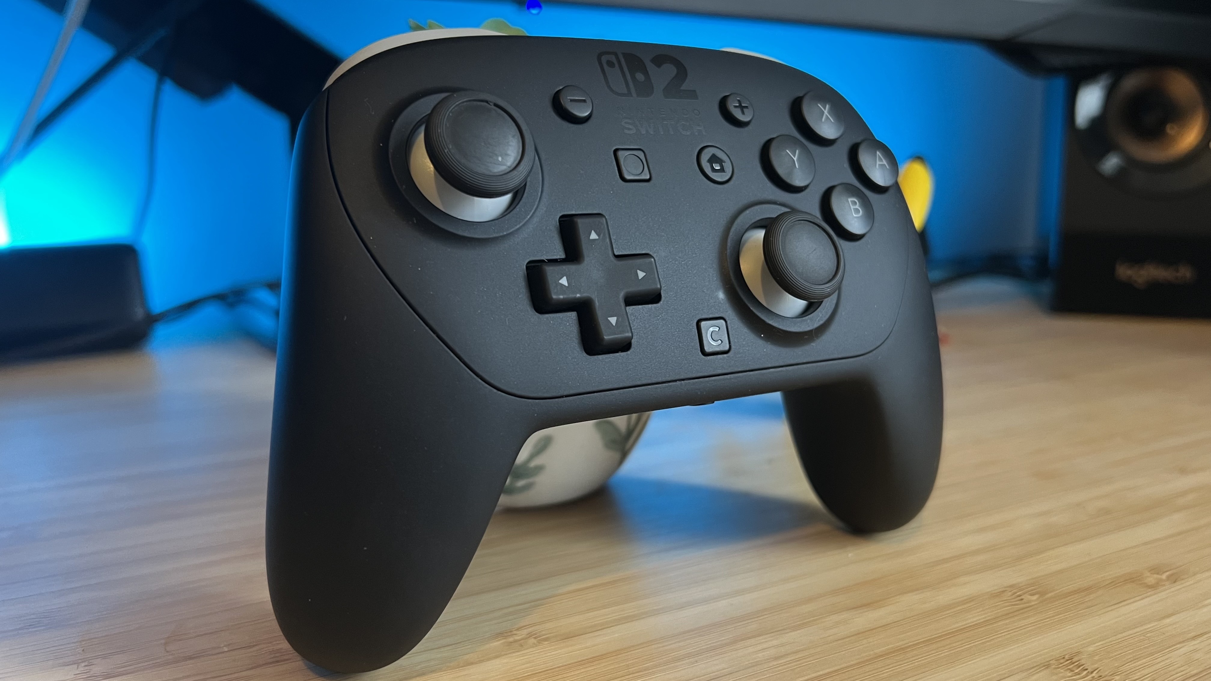 Nintendo Switch 2 Pro Controller on a wooden desk with blue backlighting