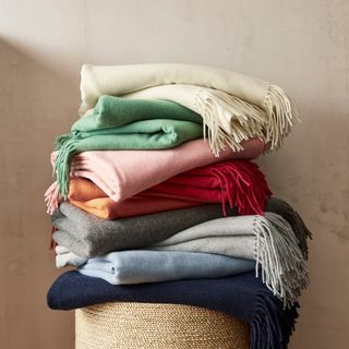 Several colors of the Williams Sonoma European Solid Cashmere Throw stacked on top of each other
