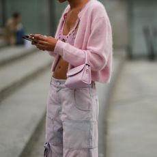 guest wears a pale pink wool cardigan, a pale pink shiny leather crocodile pattern handbag, high waist denim cargo denim large pants, a pink rhinestones checkered cut-out V-neck cropped tank-top, outside Ludovic de Saint Sernin, during Paris Fashion Week - Womenswear Spring Summer 2022, on October 03, 2021 in Paris, France