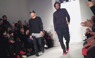 Two males modelling casual black outfits and the model on the right wears a touch of red on his shoes