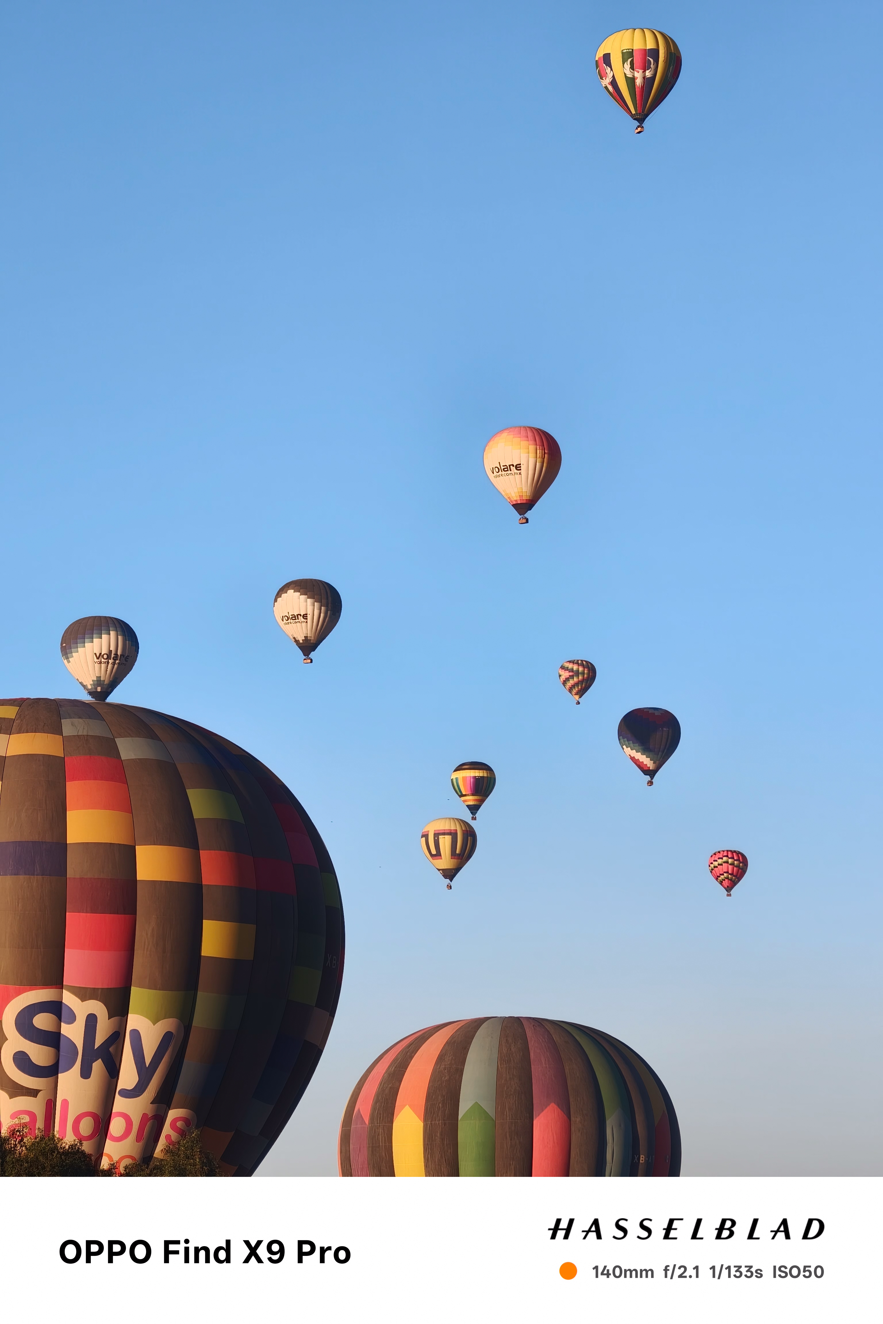 A cluster of hot air balloons in the air in front of a clear blue sky