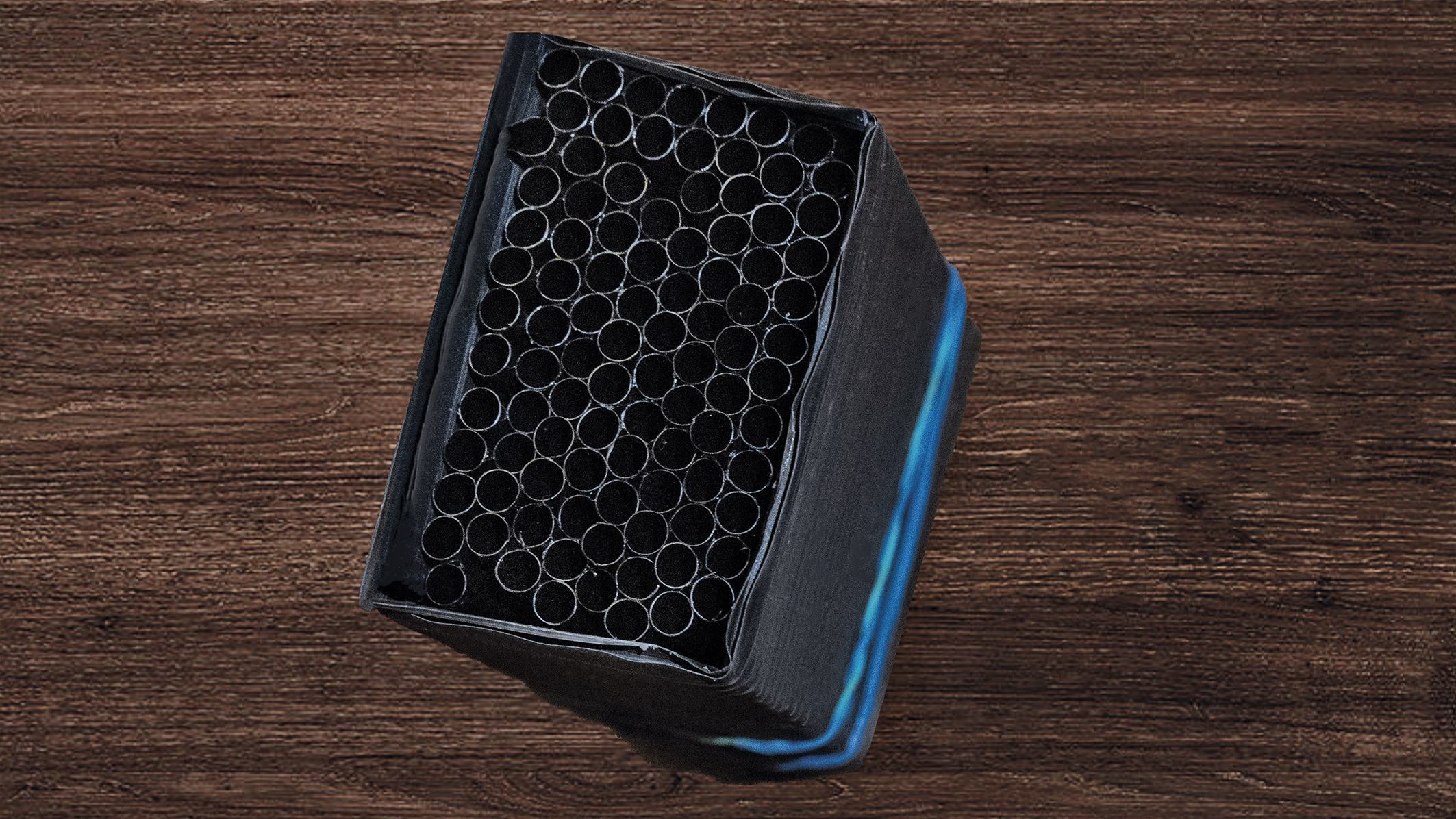Close-up of a compact black diffuser with multiple circular straws, sitting on a textured wooden surface