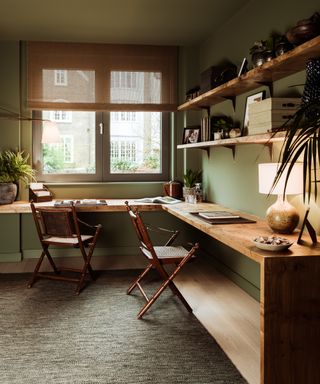 A study with green walls, wooden L-shaped desk and wooden open shelves