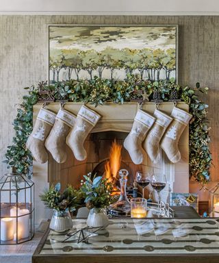 Christmas mantel decor ideas with sandstone fireplace and neutral stocking hanging from a mantel, decorated with a foliage garland