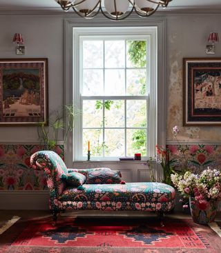 boho decor style living room with patterned chaise, paintings, wall lights, flowers, bohemian style wallpaper and rug