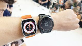 En Apple Watch Ultra runt en handled bredvid en Garmin-klocka runt handleden som jämförelse.