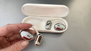 Oladance OWS open-ear earbuds in their case, held in a hand on grey background