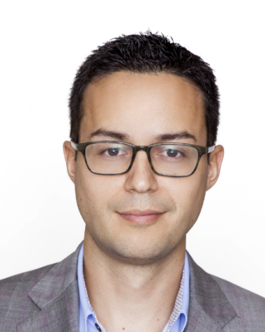 a men with dark hair and glasses wearing a gray jacket and blue shirt