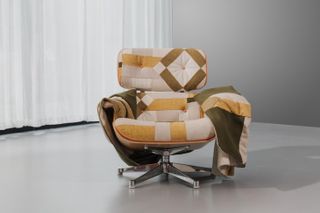 A lounge chair in the beige, brow, and orange geometrical shapes upholstery on wheels.