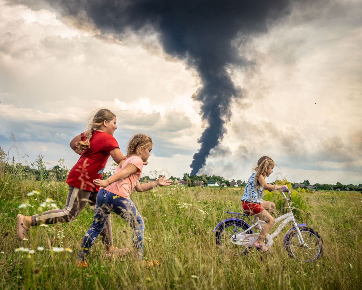 Children in Ukraine play in the foreground of a burning oil depot after last nights Russian drone strike