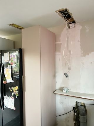 A kitchen with a black fridge and sanded walls in the process of being renovated