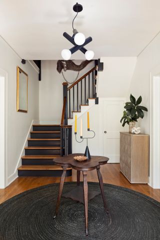 White entryway with black jute rug, dark wood rounded table, and black and dark wood staircase
