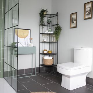 bathroom with black floor tiles, black shelving corner unit and a white toilet