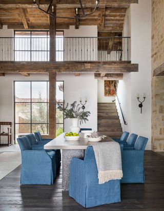 dining space with blue chairs and white topped table with mezzanine above with exposed wooden rafters and stone walls