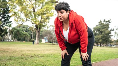 Female jogger in a park, bent over with her hands on her knees