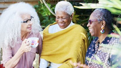 A group of three retired women laugh together outside.