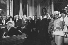 President Lyndon Johnson signs the Civil Rights Act with Dr. Martin Luther King Jr. and other leaders watching.