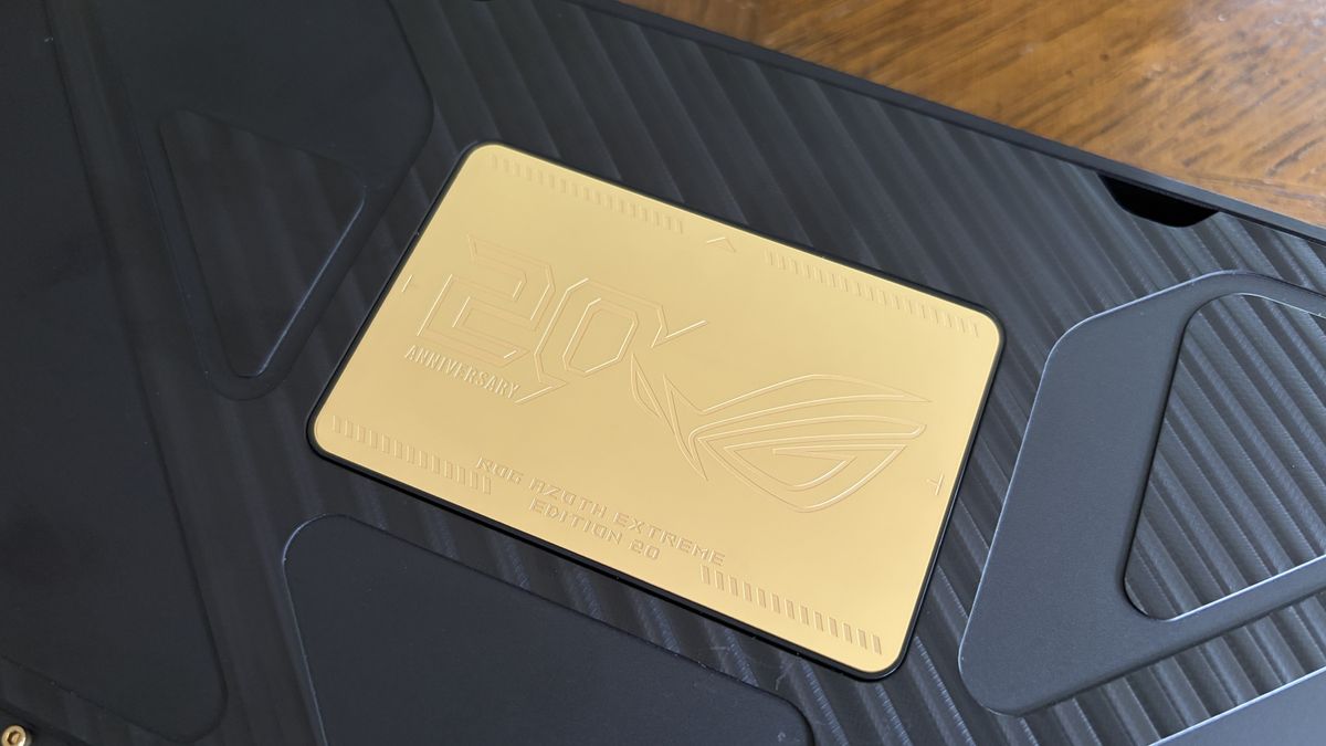 A gold plate on an ASUS ROG keyboard black textured surface with embossed text and a logo.