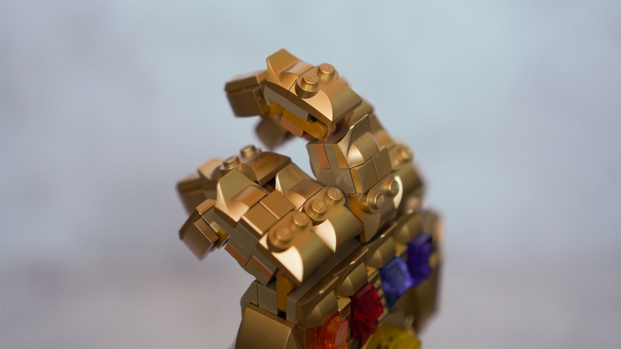 A side shot of hand made of gold bricks with multi-colored stones on the back is in front of a grey background.