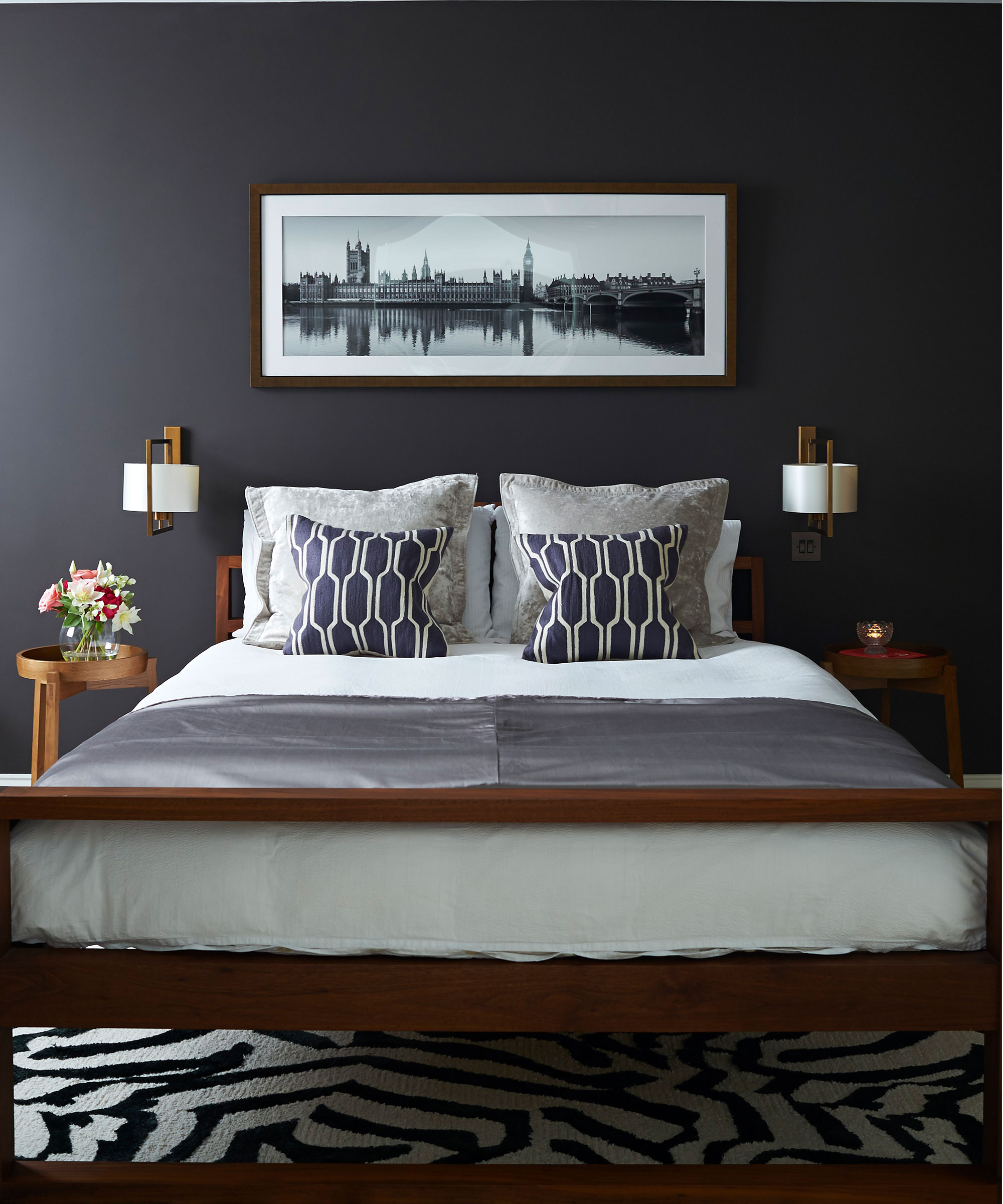 White and gold wall lamps on either side of a dark bed with white and blue cushions.