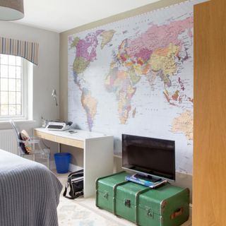 Teenage bedroom with world map mural, white desk, vintage green suitcase.