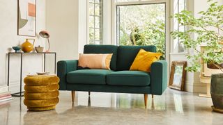 A green velvet sofa in a lounge accessorized with cushions to illustration the forest green color trend