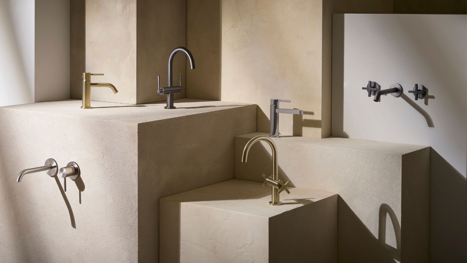 Minimalist bathroom tap display showing wall-mounted and deck-mounted taps in brass, chrome and black finishes on textured stone plinths.