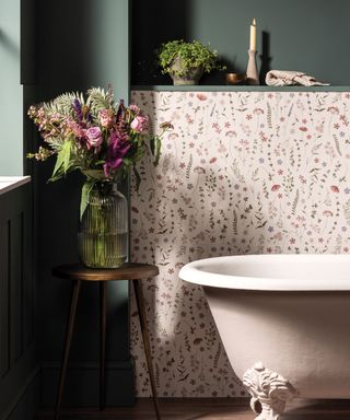 Small bathroom with decorative meadow flower tiles and contrast dark green wall, and light pink roll-top bath