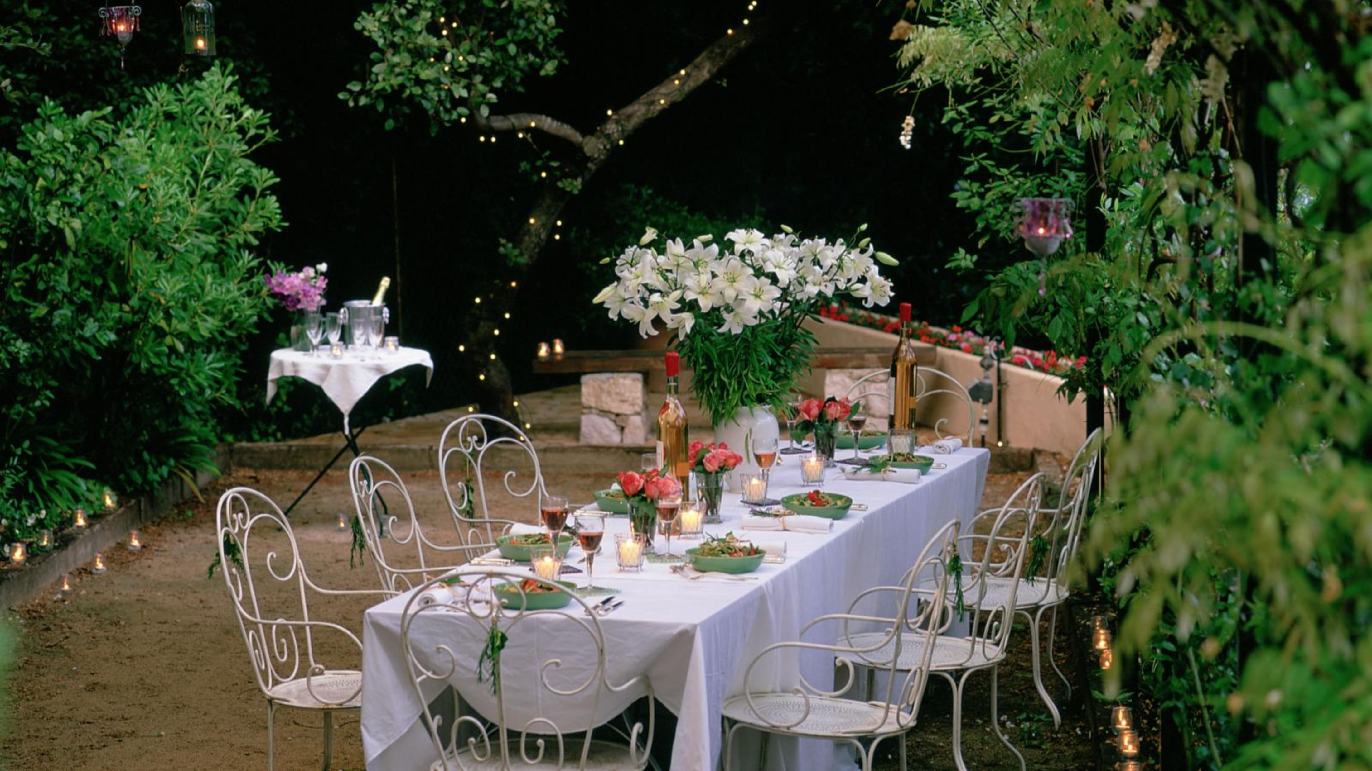 Whimsical garden party tablescape just before sunset, softly lit by flowing string lights hanging overhead