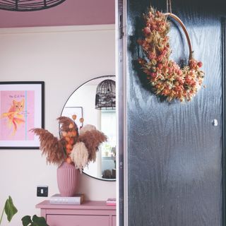 A pink hallway with an autumn wreath adorning the home's open black front door