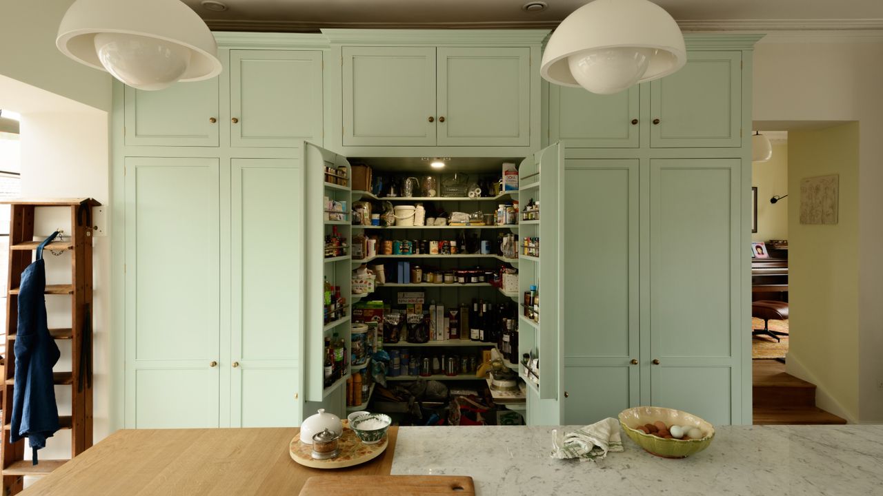 green pantry built into cabinetry with open doors, kitchen island in foreground, marble topped, lighting