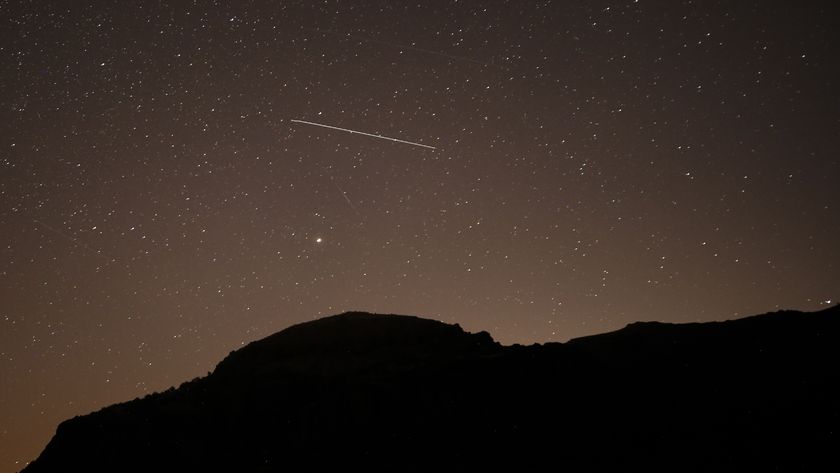 A lone meteor is spotted streaking through a dark starry sky above a silhouetted hill.
