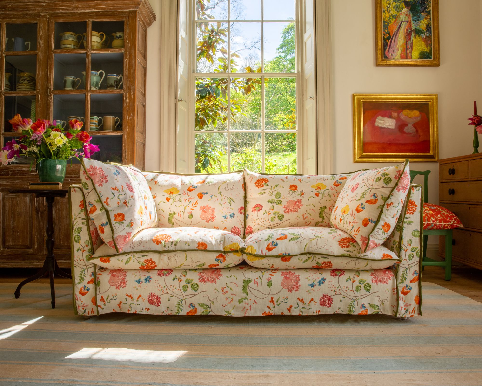 A cream sofa with a large colourful floral print overlay sitting on a pale blue and cream striped rug