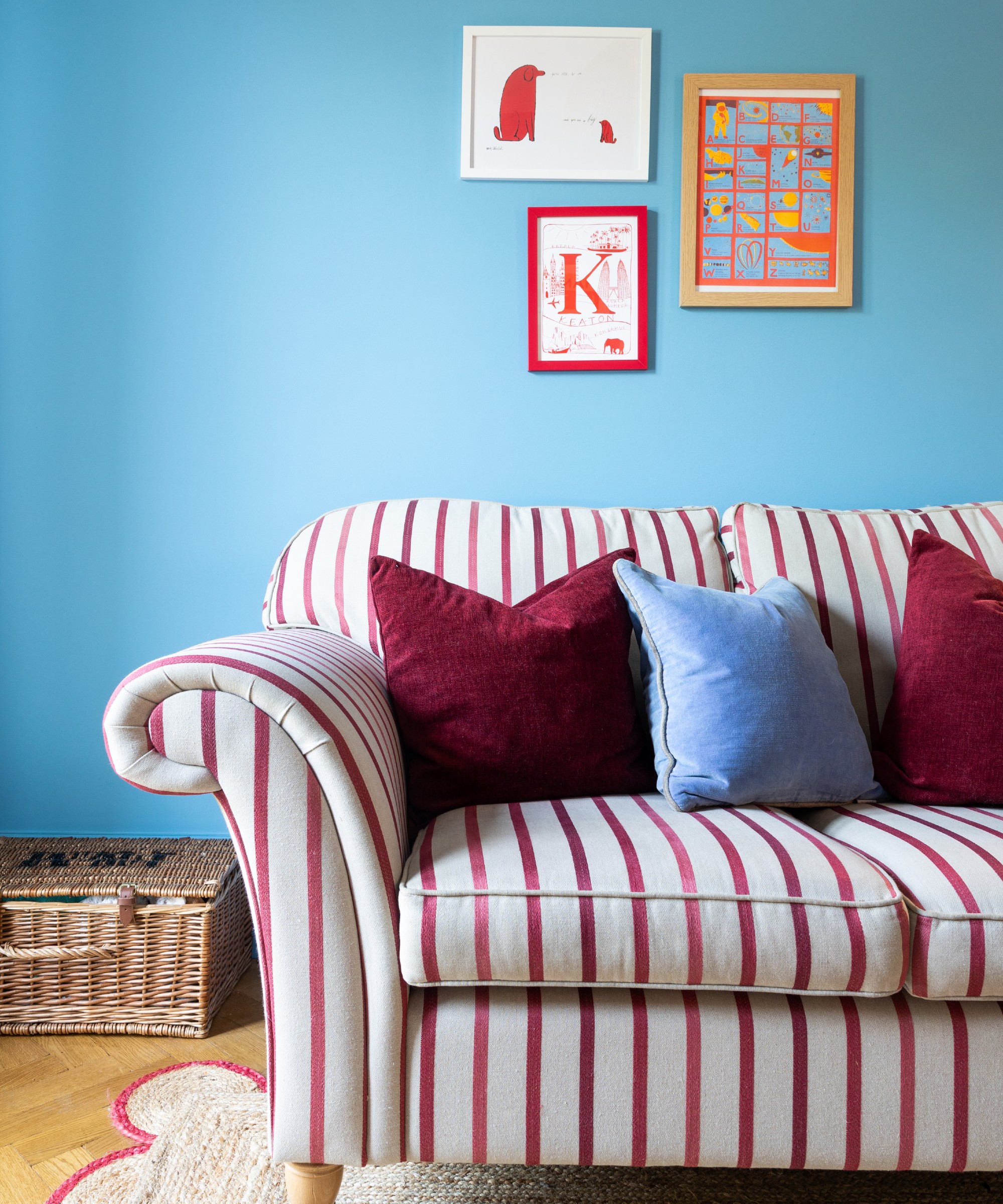 A blue-painted living room with a striped dark red sofa and blue and red velvet cushions