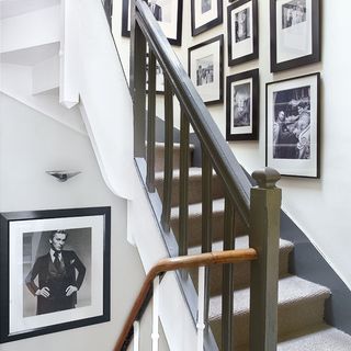 carpeted stairs with stair runner, wood banisters and white walls with black and white framed photos