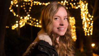 A woman smiling with fairy lights behind