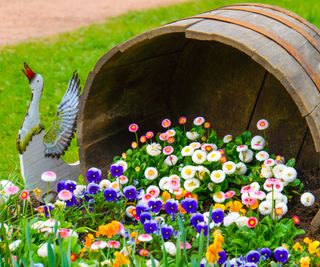 Flowers spilling out of a sideways barrel next to a wooden goose sculpture
