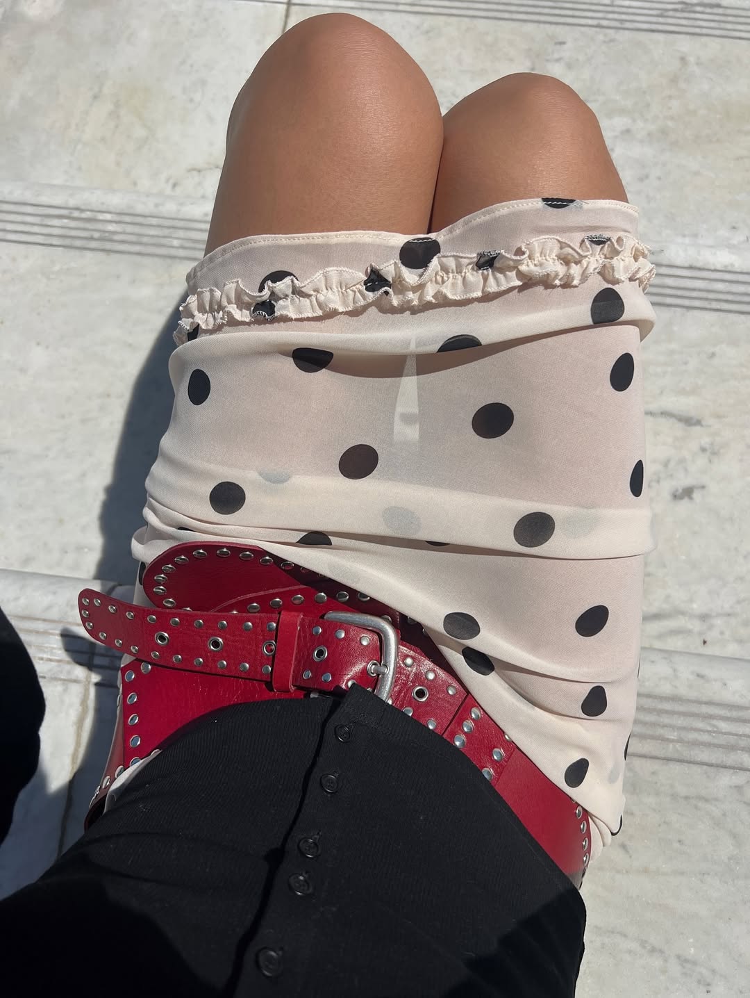 @shhtephs wears a sheer white-and-black polka dot skirt with a red belt and black cardigan
