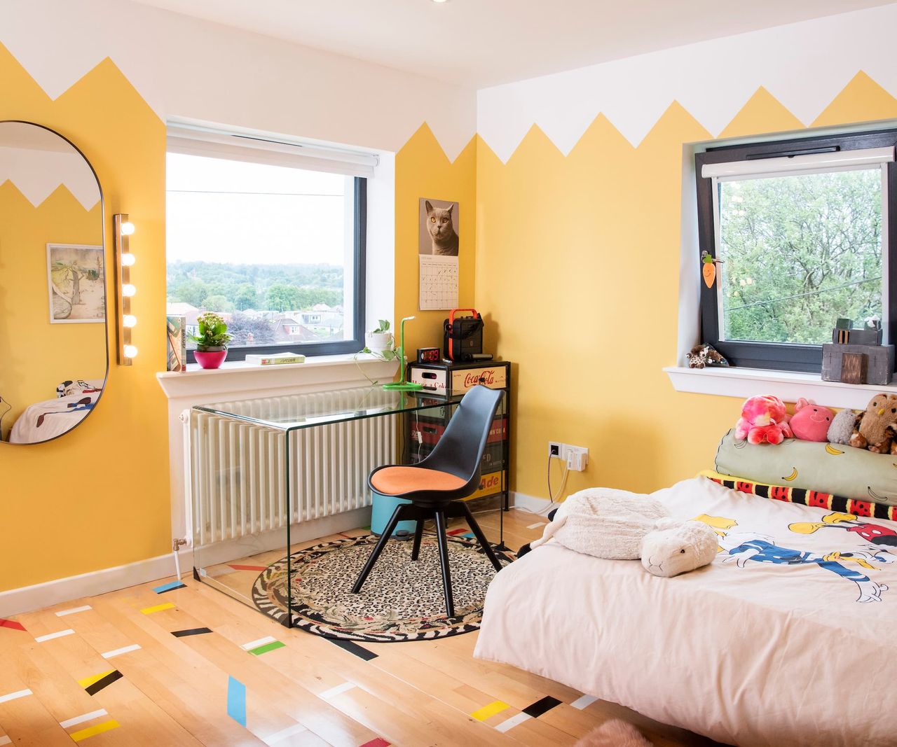 A yellow walled bedroom with a glass desk
