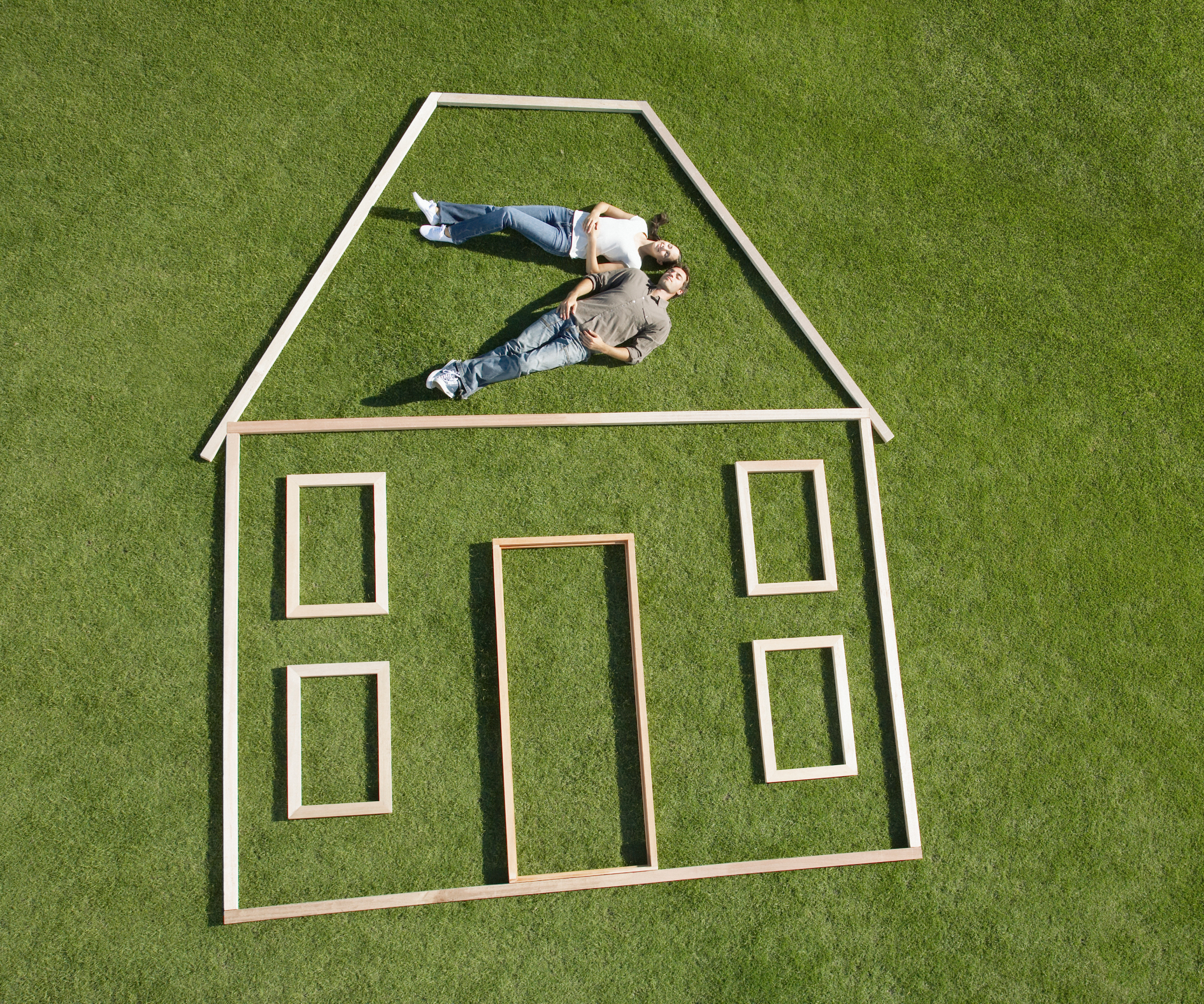 outline of house in wood strips placed on floor with couple lying on grass in roof section