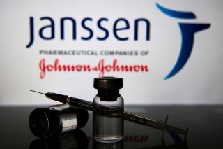 An image of two vials and a syringe in front of Johnson and Johnson's Janssen pharmaceutical companies sign.