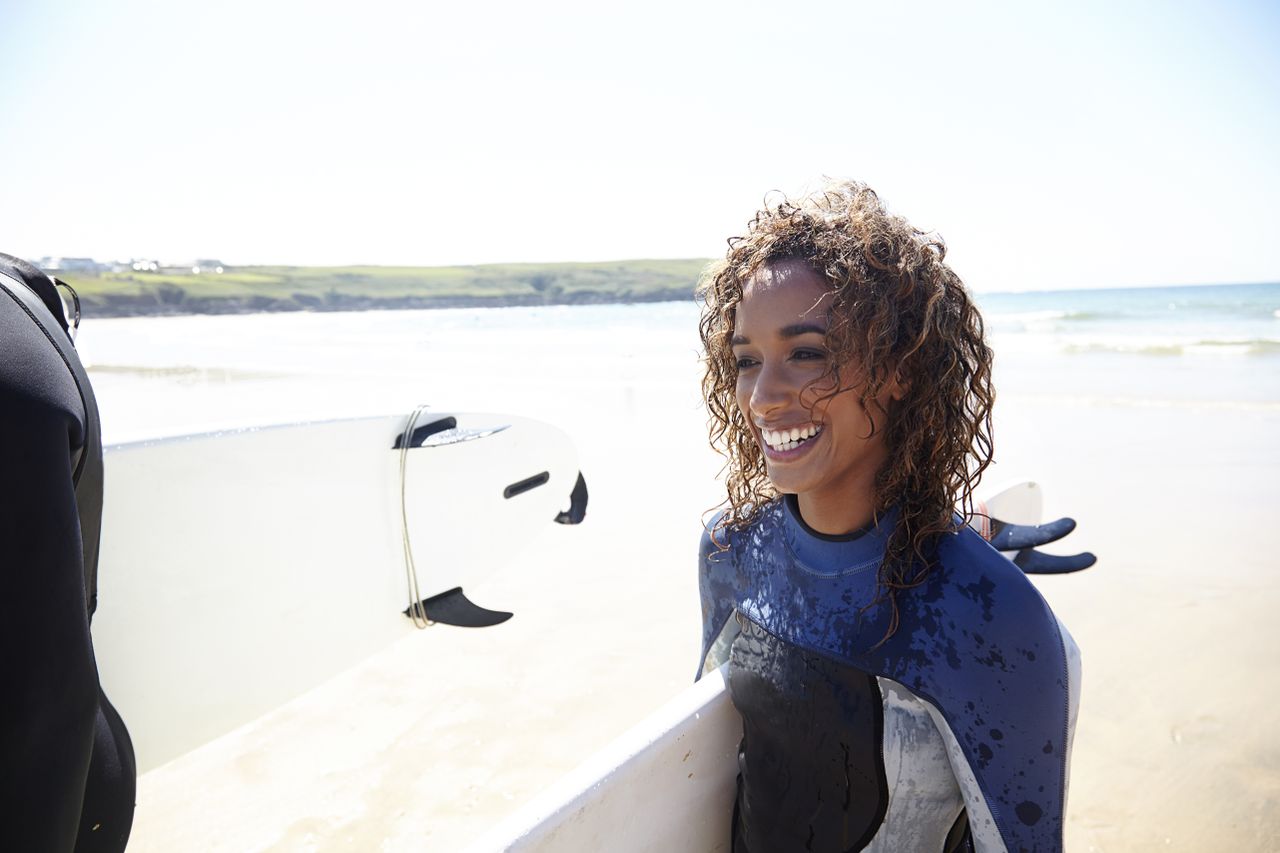 Smiling woman with surfboard walking on the beach – an example of habits for happiness