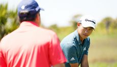 Collin Morikawa stares back at his coach whilst addressing the golf ball
