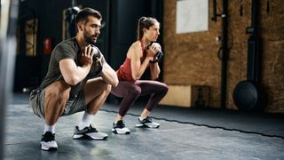 Man and woman in gym performing goblet squats with kettlebells