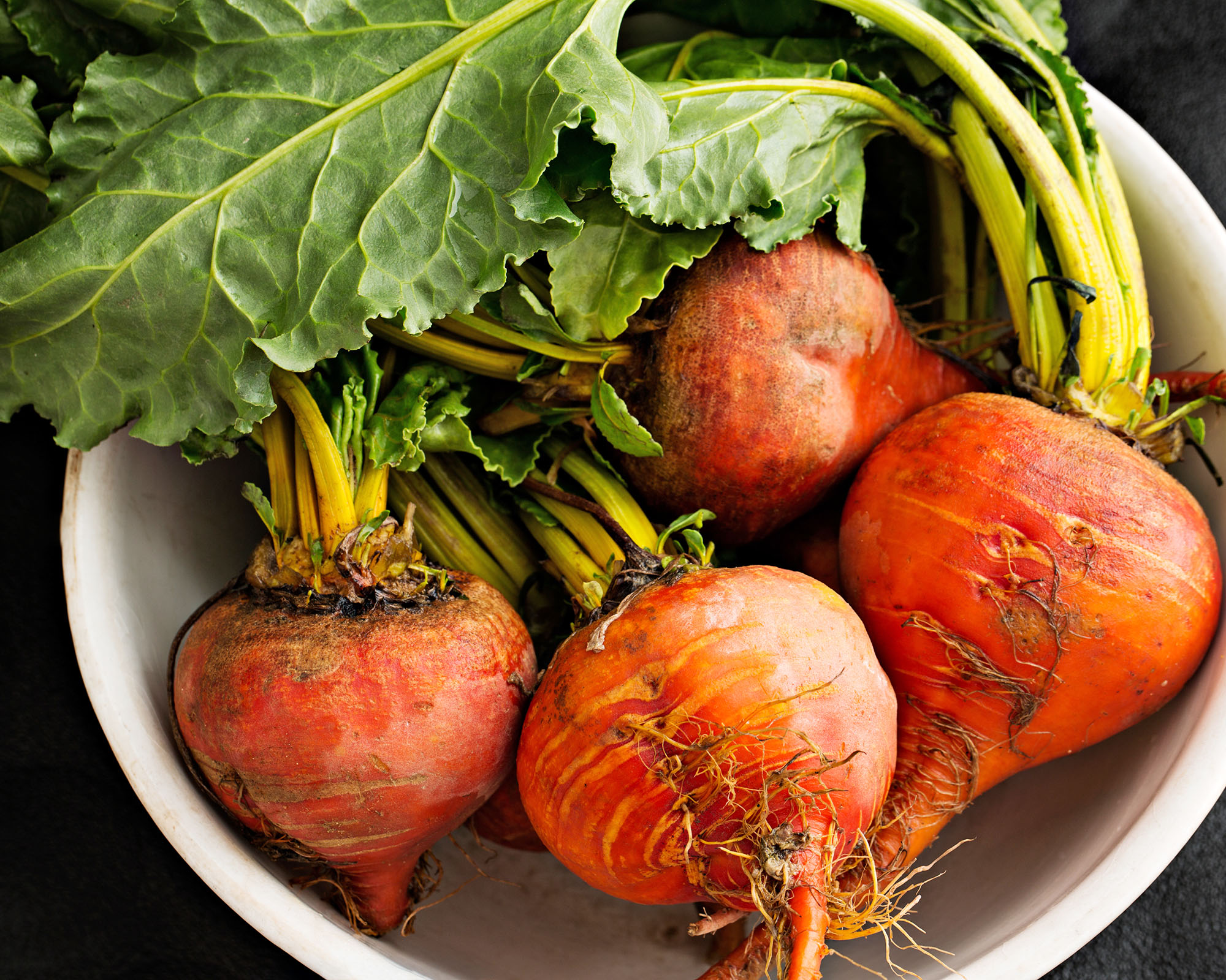 An overhead close up shot of some freshly picked golden beets in an old bowl